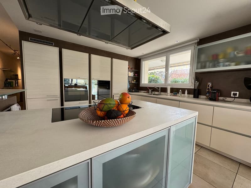 Modern kitchen with white cabinets, a central island, and a fruit bowl on the counter. Features include an oven, sink, and ample storage space.