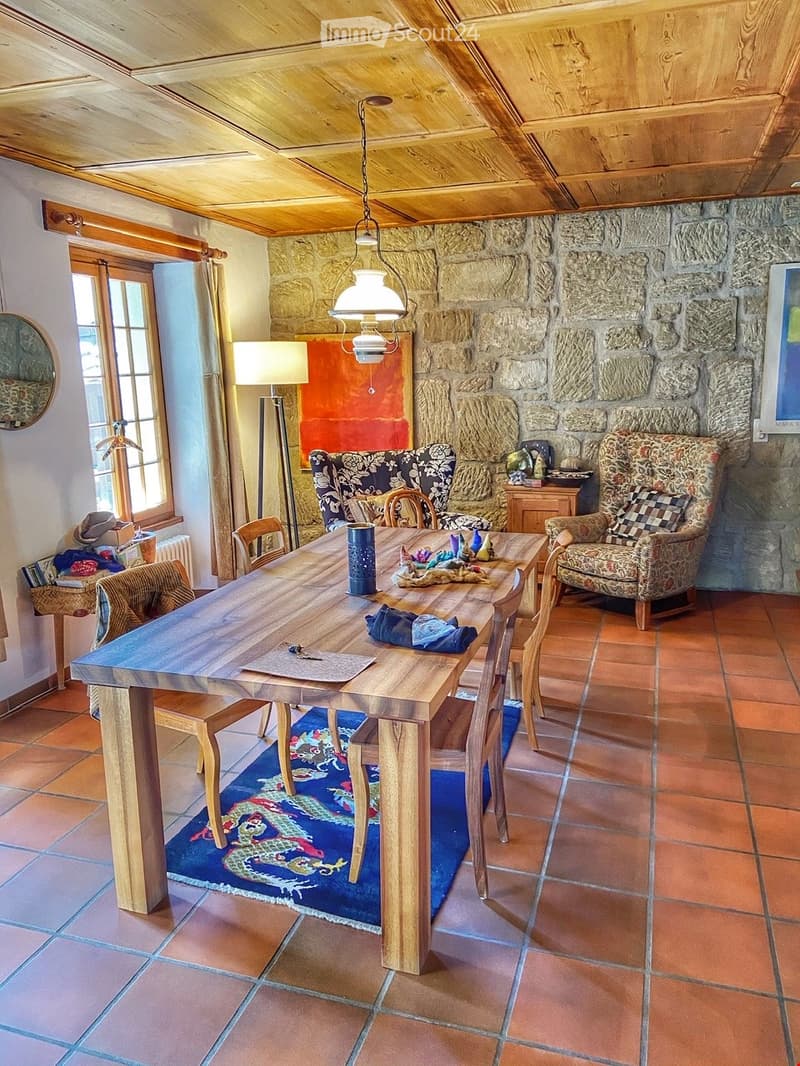 Dining room with wooden dining table, chairs, armchairs, floor lamp, pendant light, and a stone wall.