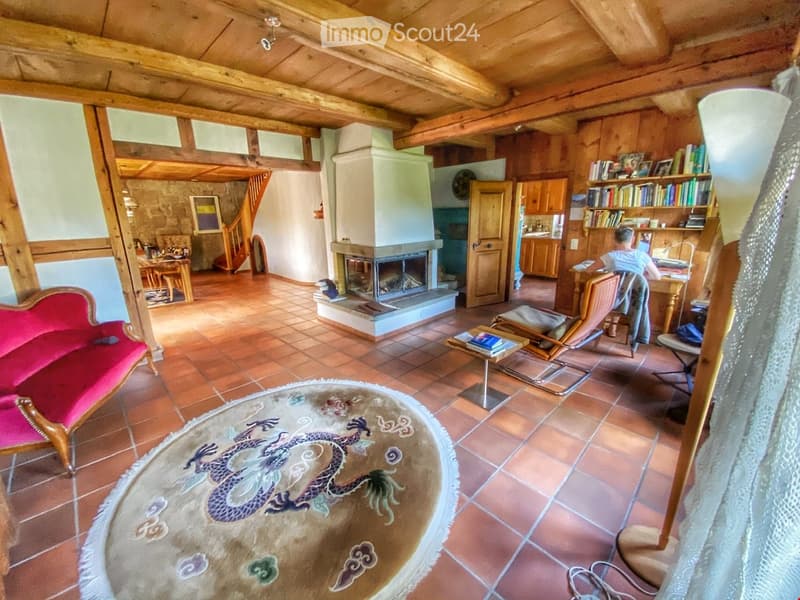 Cozy living room with exposed wooden beams, fireplace, red sofa, coffee table, and bookshelves.