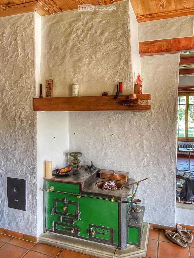 A rustic kitchen with a green stove, wooden shelf, and various decorative items including a candle, plate, bowl, and statue.