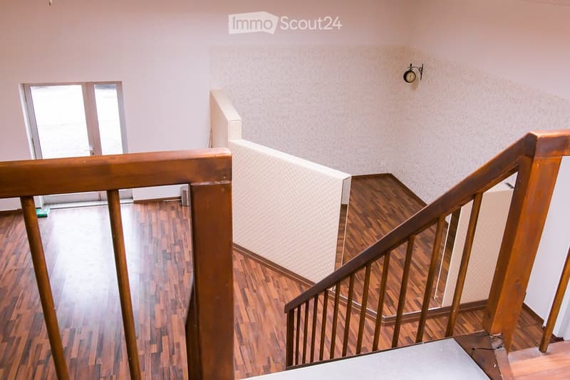 Wooden staircase with a polished wooden railing and a wooden floor, leading to an open doorway with glass panels.