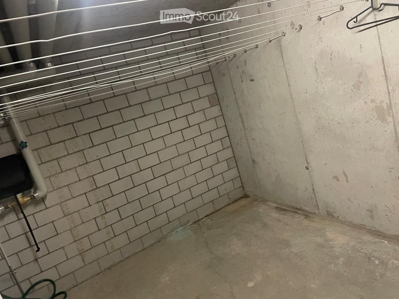 Empty utility space with concrete floor, brick wall, exposed pipes, and a clothes drying rack.