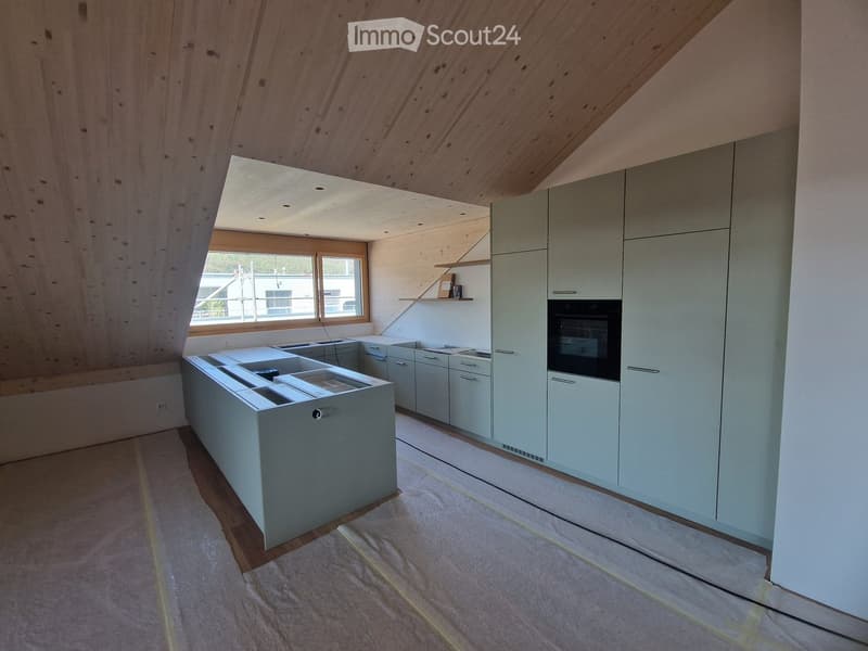 Modern kitchen with light grey cabinets, a central island with a sink, and an oven. The space features wooden walls and a skylight, with a window offering a view of the outside.