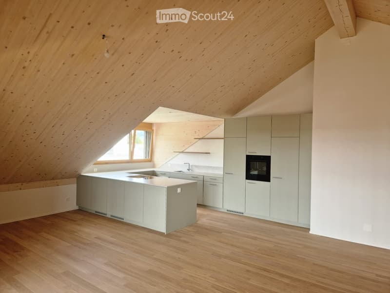 Modern kitchen with light grey cabinets, a central island, and wooden flooring, featuring a skylight and large window for natural light.