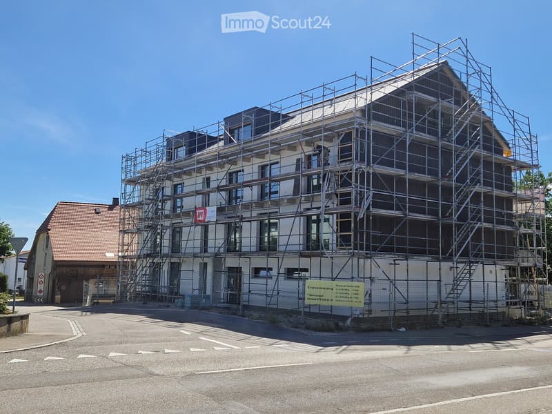 Multi-story building under construction with scaffolding, visible windows, and a signboard on the ground floor.