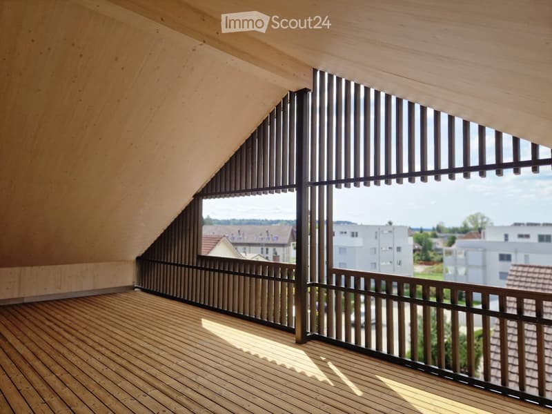 Wooden balcony with slatted railing and large windows overlooking a residential area.