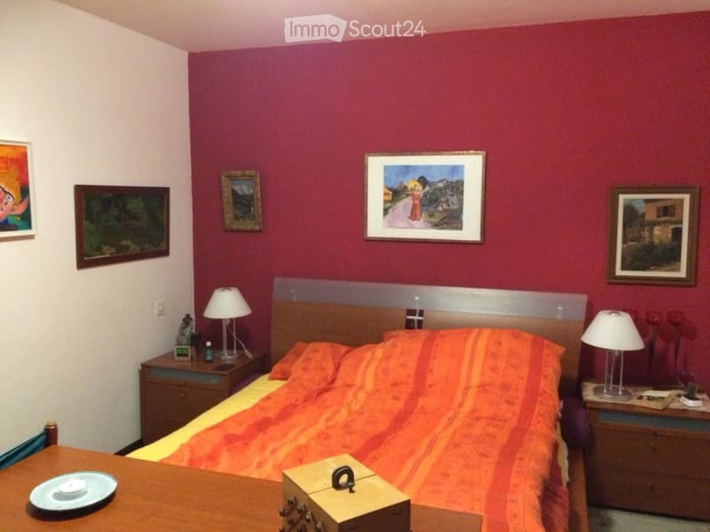 Bedroom with a large bed, orange and yellow bedding, two nightstands with lamps, a small table with a plate, and several framed pictures on the walls.