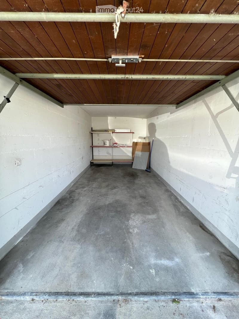 Empty garage with concrete floor, white walls, wooden ceiling, and minimal storage shelves.