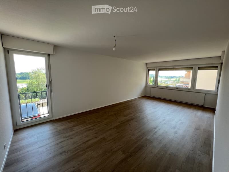 Empty room with wooden flooring, large windows, and a sliding glass door leading to a balcony.