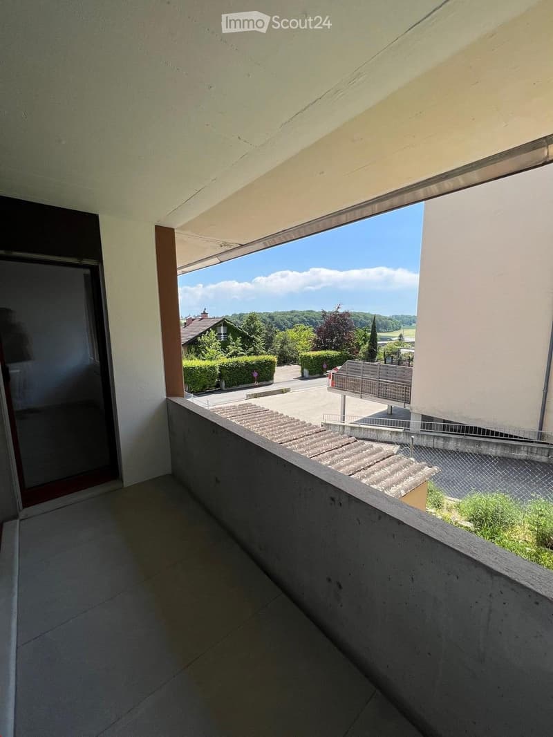 Balcony with tiled floor, concrete railing, and a view of a green landscape and buildings.