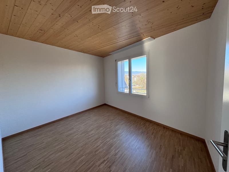 Empty room with wooden flooring, white walls, and a large window offering a scenic view.