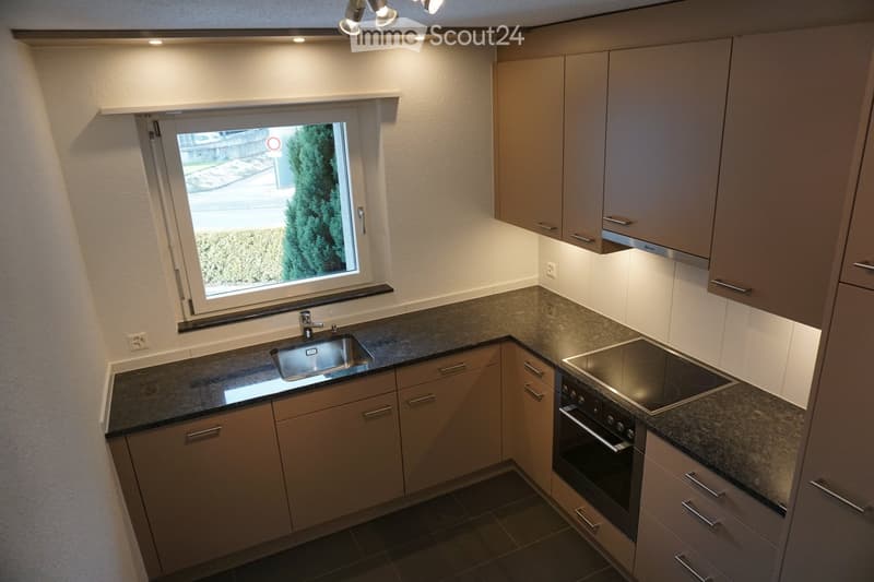 Modern kitchen with light-colored cabinets, granite countertops, a sink, and an electric stove with an oven below.