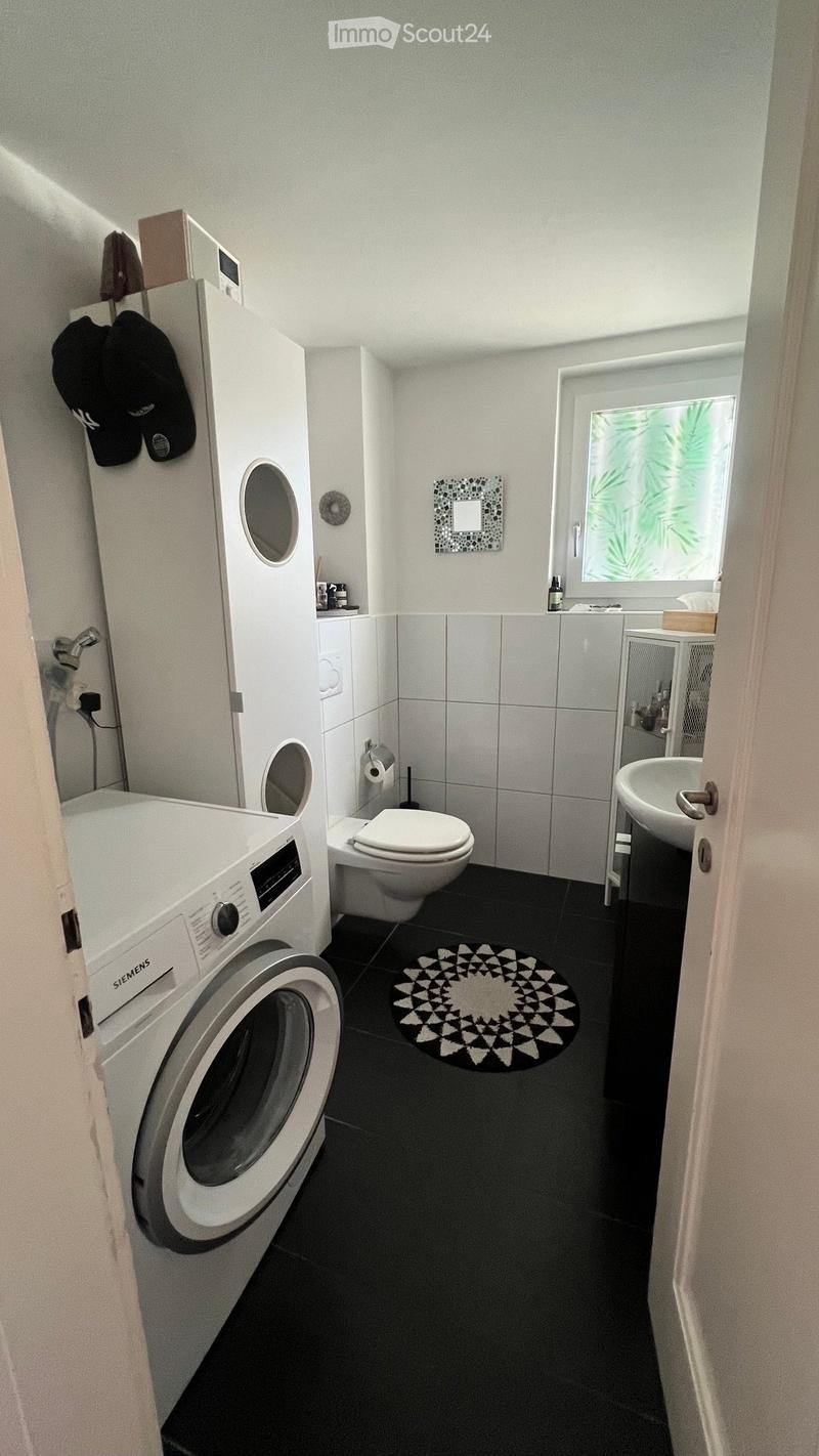 Modern bathroom with black tiled floor, white washing machine, toilet, sink, and a decorative black and white circular rug.