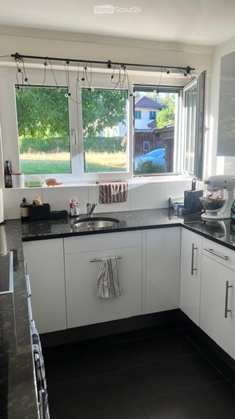 Modern kitchen with white cabinets, black countertop, stainless steel sink, mixer, and towels hanging from cabinet handles.