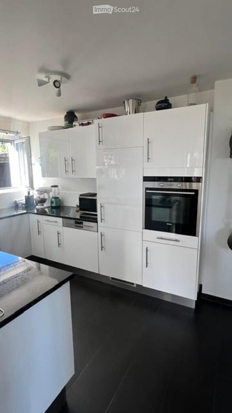 Modern kitchen with white cabinets, black countertops, and black floor. Features a built-in oven, microwave, and refrigerator. A blender is placed on the counter.
