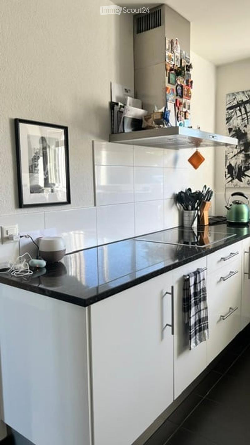 Modern kitchen with white cabinets, black countertop, stainless steel appliances, and a range hood. Includes a framed picture on the wall and a kitchen towel hanging from a cabinet handle.