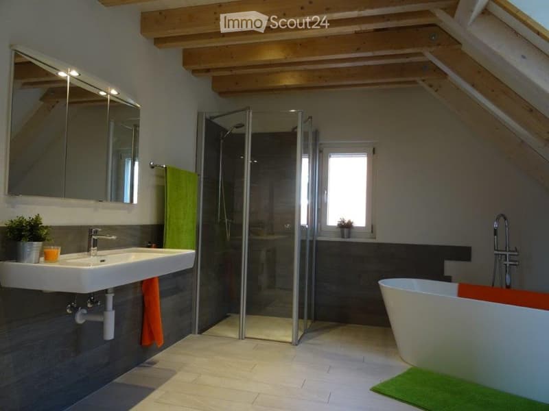 Modern bathroom with a white sink, bathtub, large mirror, glass-enclosed shower, and wooden slanted ceiling beams.