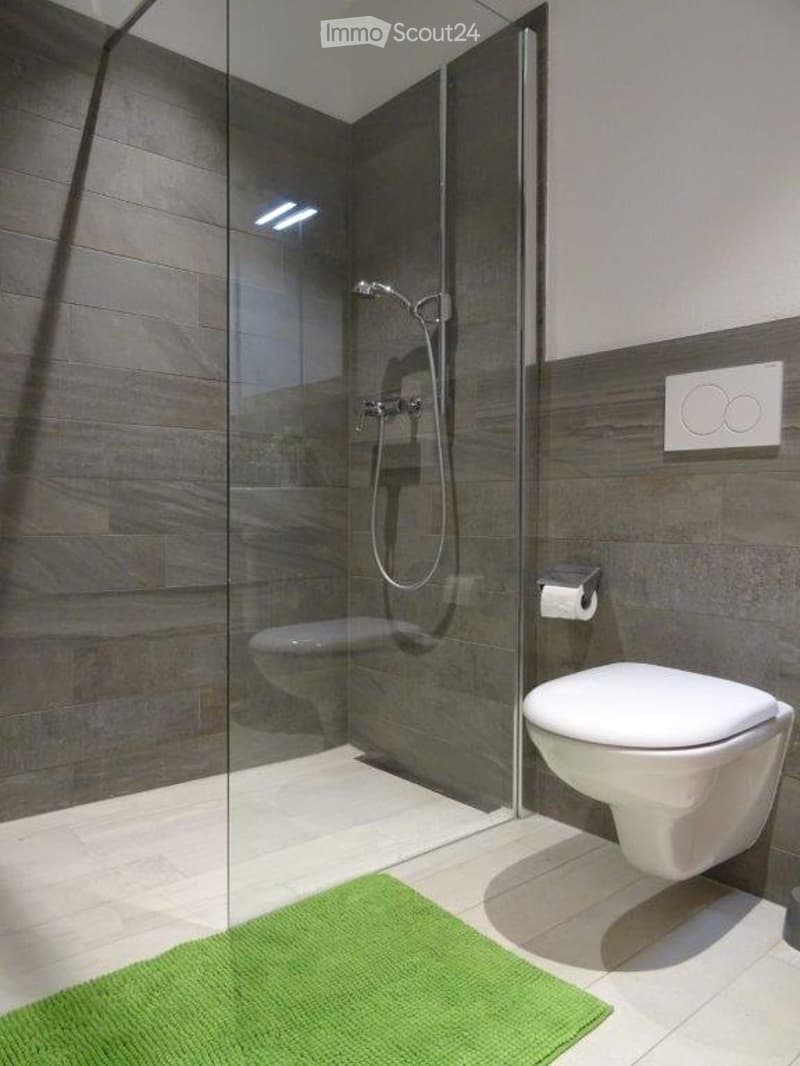 Modern bathroom with a glass-enclosed shower, a toilet, and a green bath mat on the floor.