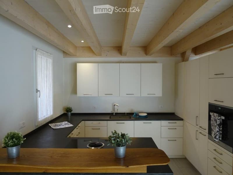 Modern kitchen with white cabinets, black countertops, and a wooden island. Features include a sink, stove, oven, and small potted plants on the counter.