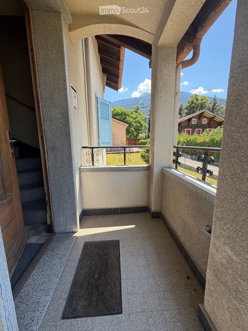 Balcony with stone walls, tiled floor, metal railing, and a view of a green lawn and mountains.
