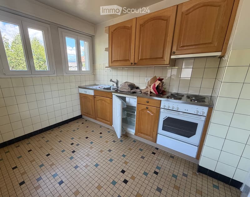 Kitchen with wooden cabinets, tiled walls, and a countertop with a sink, stove, and oven. There are also some items on the counter, including a bag and a flower arrangement.