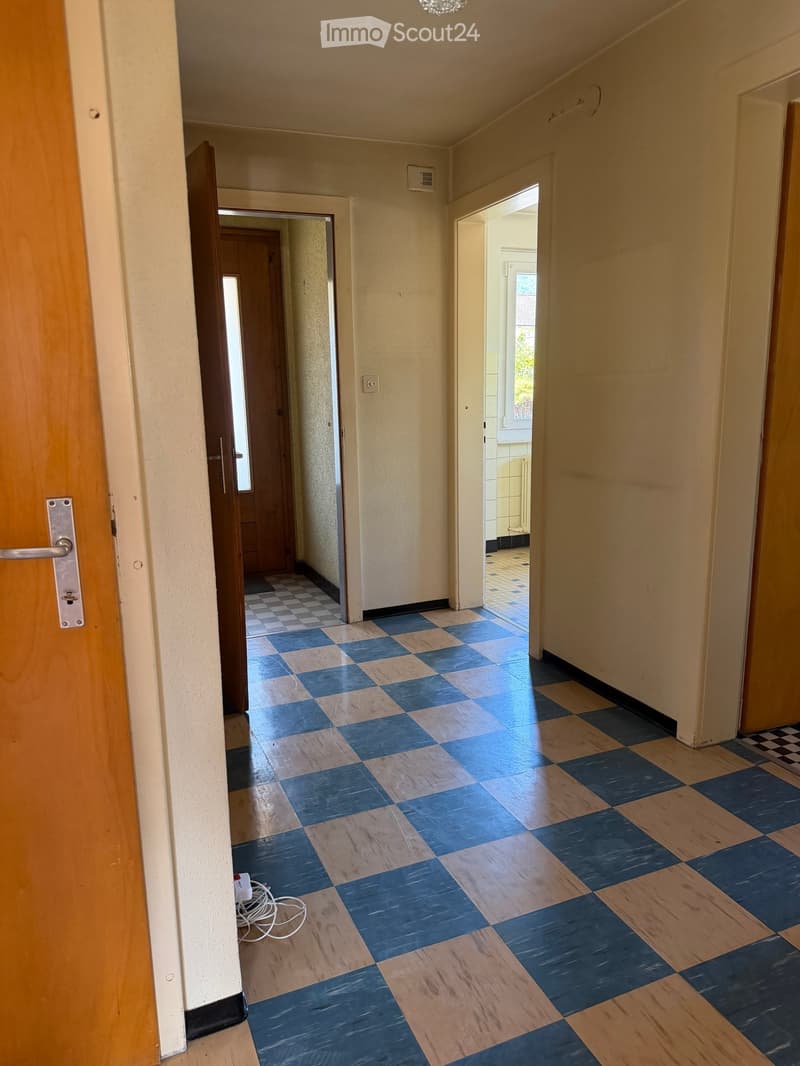 Empty hallway with checkered blue and beige tiles, cream-colored walls, and open doors leading to other rooms.
