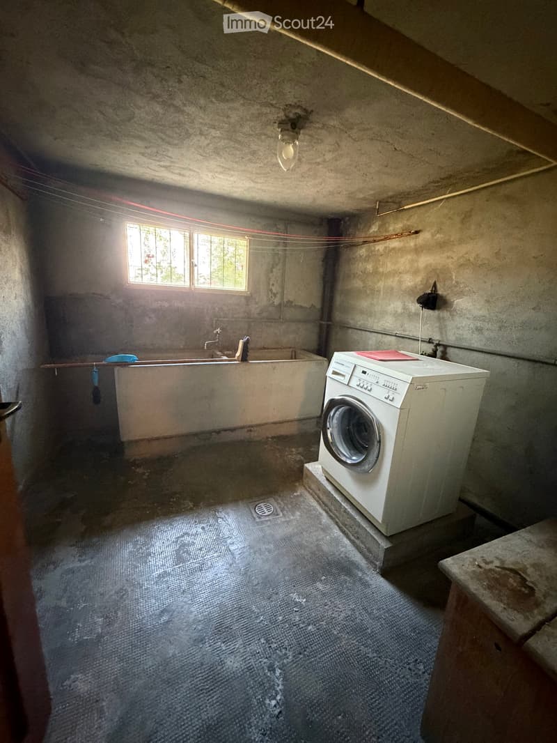Concrete-walled bathroom with a washing machine, bathtub, and small window providing natural light.