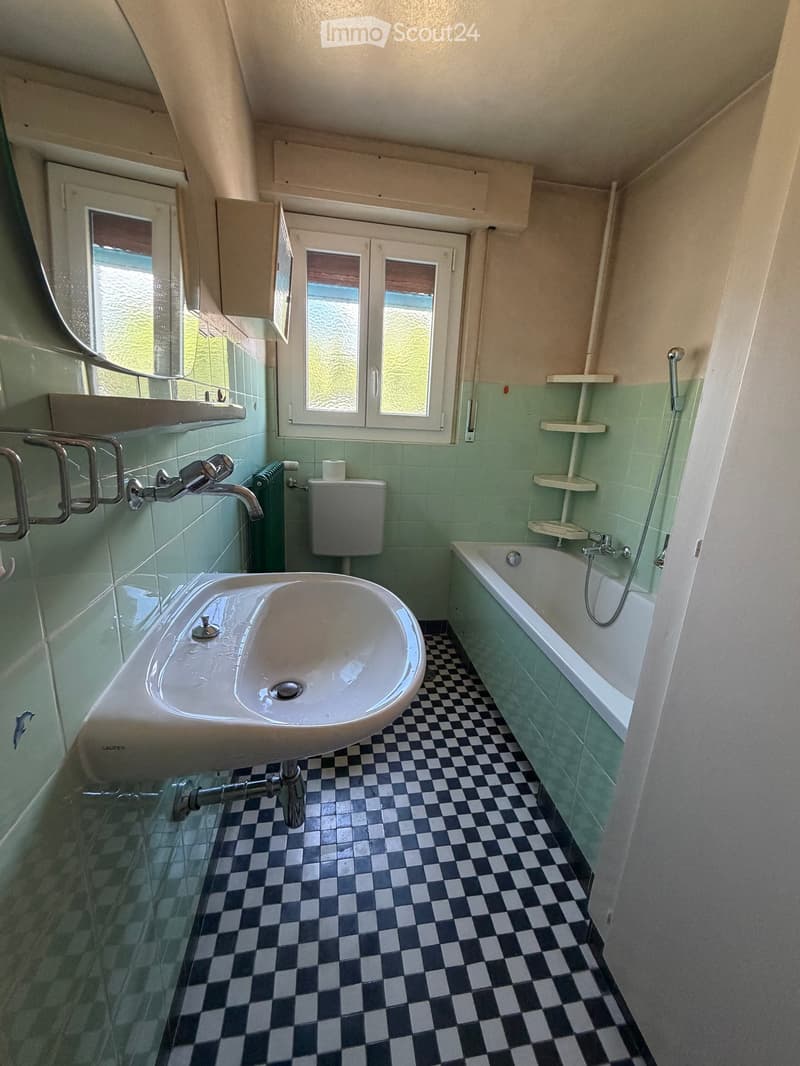 Bathroom with green tiled walls, checkered black and white floor, sink, bathtub, toilet, and shelves.