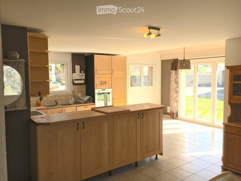 Bright kitchen with a central wooden island, sink, oven, and ample cabinetry. Large windows and sliding doors lead to a green outdoor area.