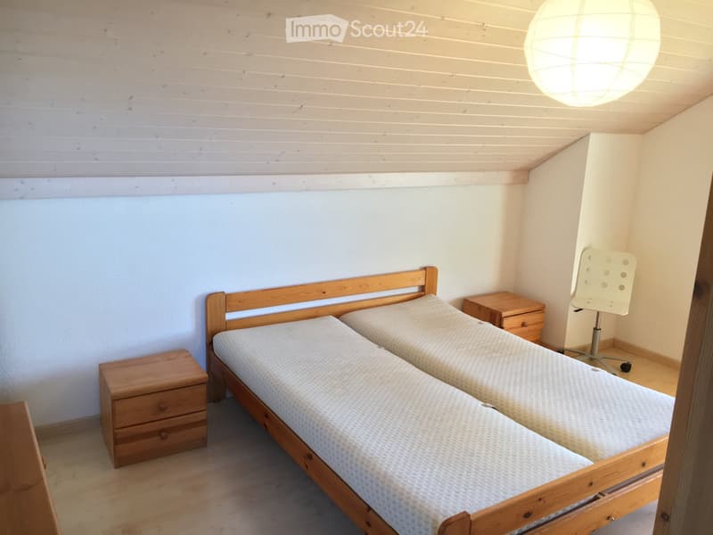 Cozy bedroom with two single beds, wooden nightstands, a white chair, and a hanging paper lantern light fixture.