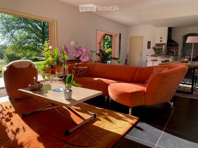 Bright living room with large windows, orange sectional sofa, coffee table, side table, and decorative plants.