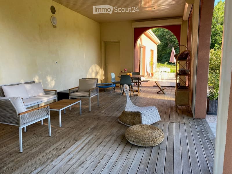 Wooden decked balcony with white sofa, chairs, a small table, and woven baskets.
