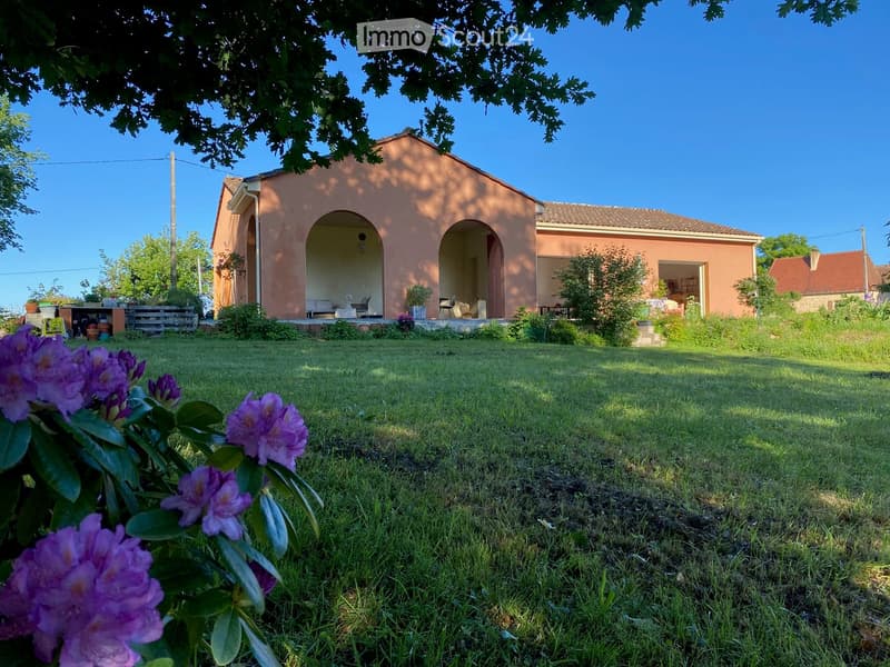Pink house with arched entrances, surrounded by a grassy lawn and trees, with visible outdoor seating and potted plants.