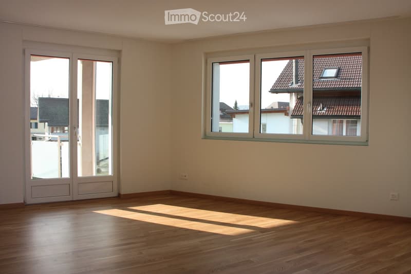 Empty room with wooden flooring, large windows, and sliding glass doors leading to a balcony.