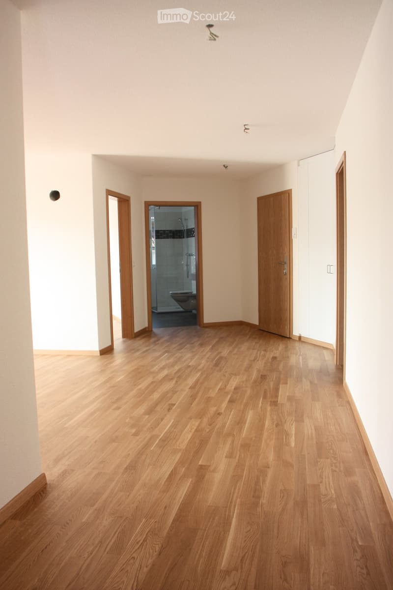 Empty room with light wooden flooring, white walls, and several doors leading to other spaces, including a bathroom.