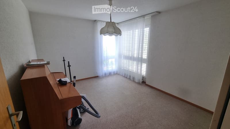 Empty room with a wooden table, a hanging lamp, and a vacuum cleaner on the floor.