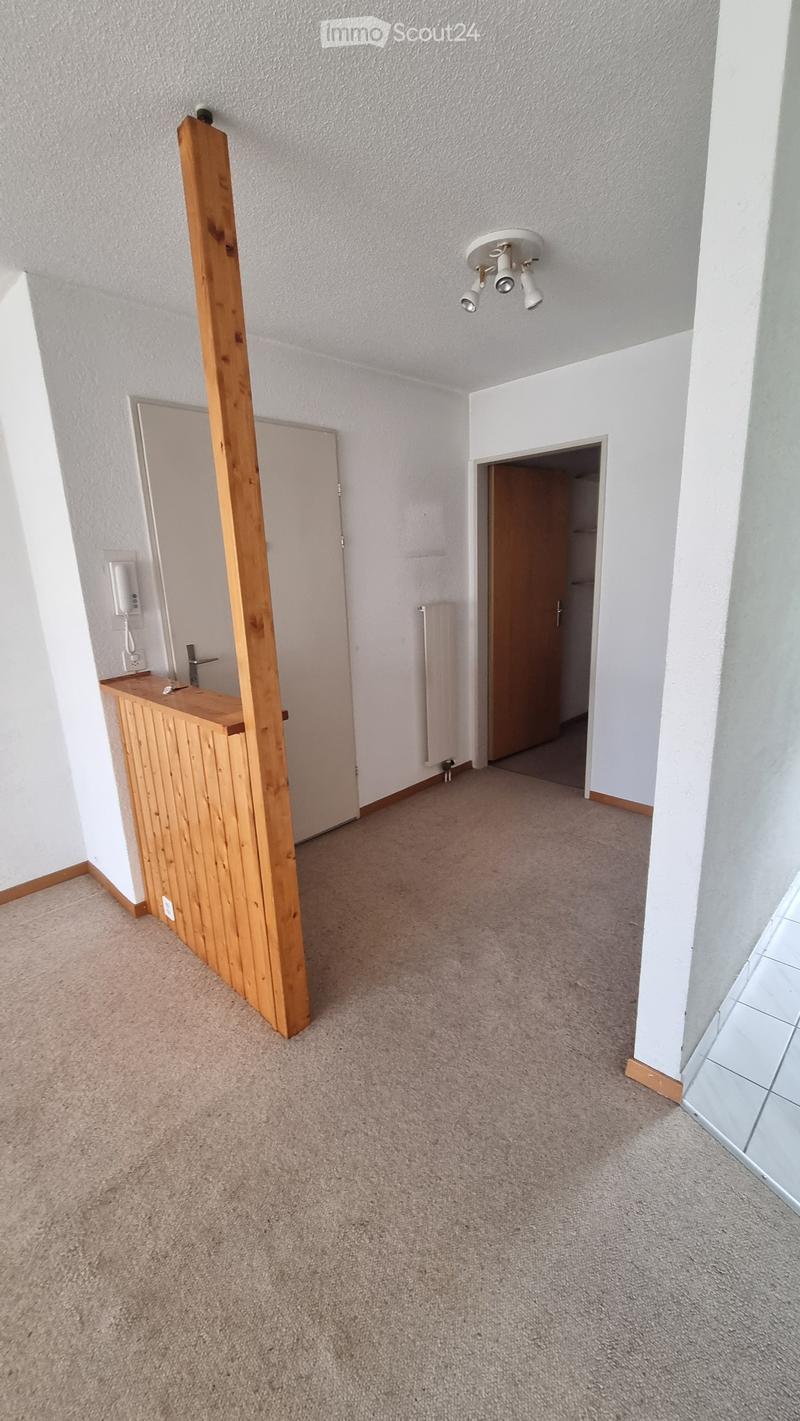 Empty room with beige carpet, white walls, and a wooden cabinet. There is a doorway leading to another room and a small wooden structure in the corner.