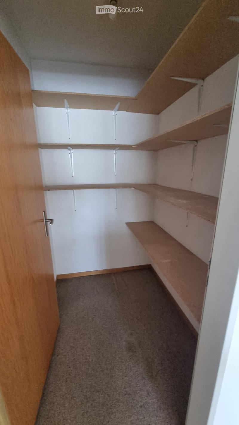 Empty closet with built-in wooden shelves and white cabinet doors, carpeted floor, and a wooden door frame.