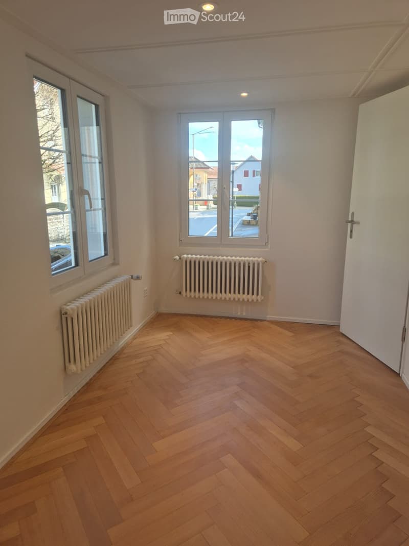 empty room, wooden parquet floor, white walls, two windows, two radiators, open door