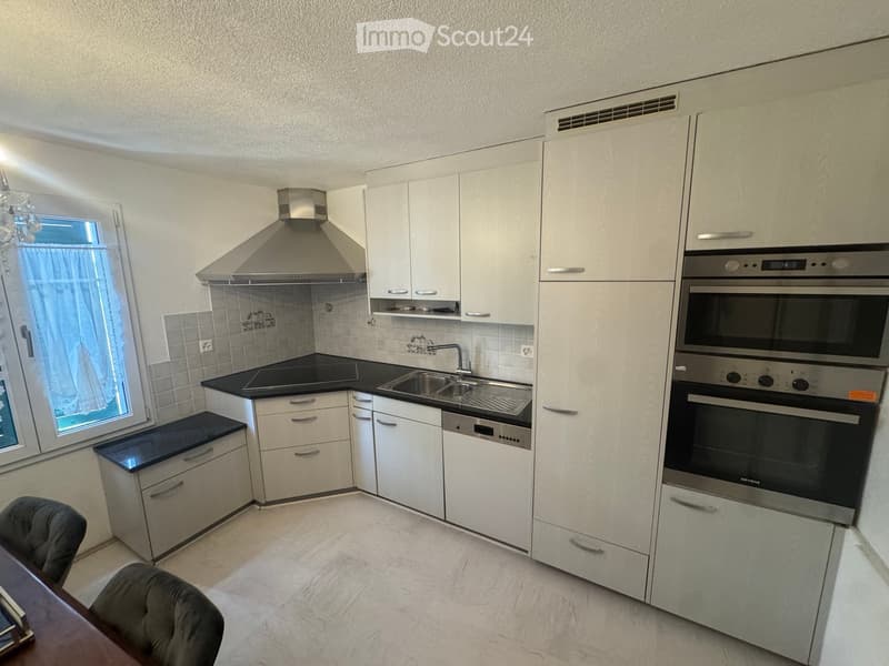 Modern kitchen with white cabinets, black countertops, stainless steel appliances, and a window with a curtain.