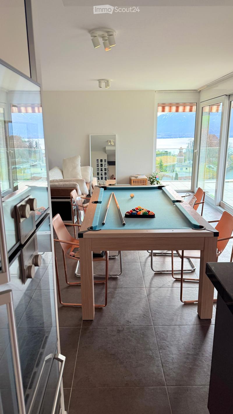 Modern living room with large windows overlooking a scenic view, featuring a pool table, comfortable seating, and decorative elements.