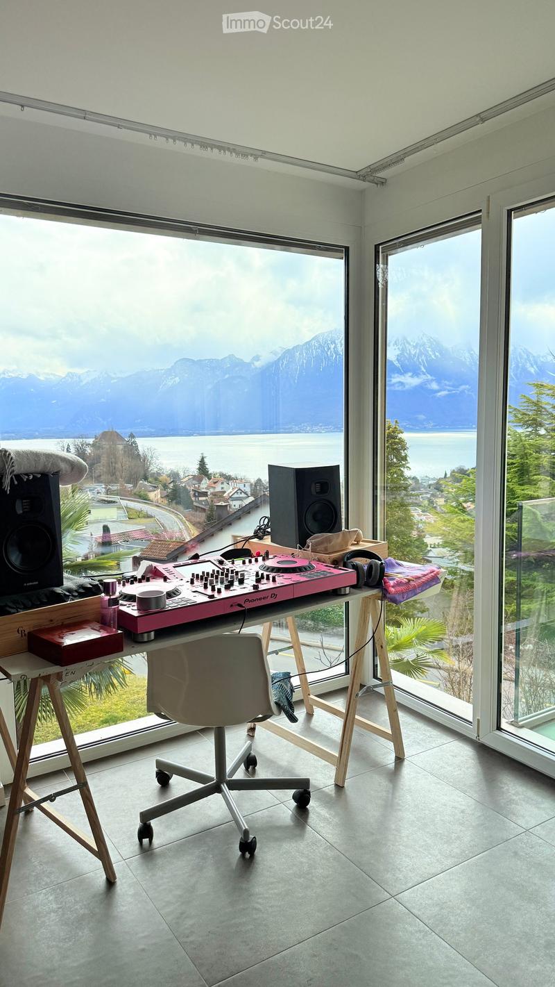 Modern room with large windows offering a scenic mountain and lake view, equipped with a DJ turntable, speakers, a chair, and a table.