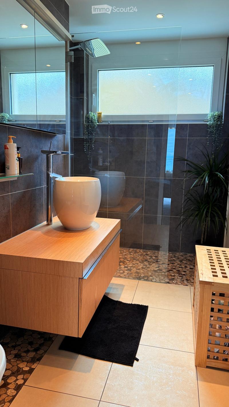 Modern bathroom with a wooden vanity, large sink, glass-enclosed shower, and a black bath mat.