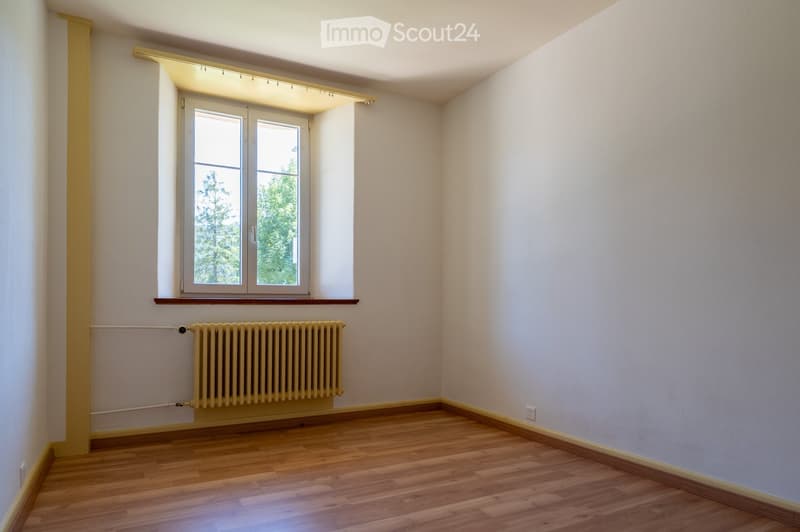 Empty room with wooden flooring, white walls, a window with double glass panes, and a radiator below the window.