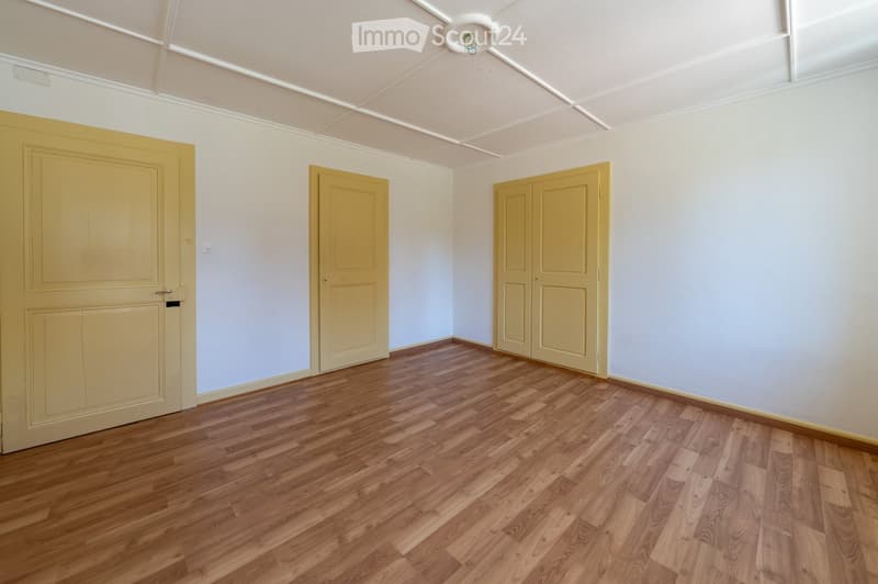 Empty room with wooden flooring, white walls, and three yellow doors.