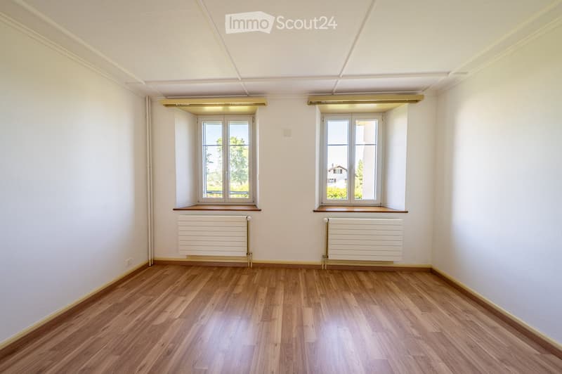 Empty room with wooden flooring, white walls, and two large windows with radiators beneath them.