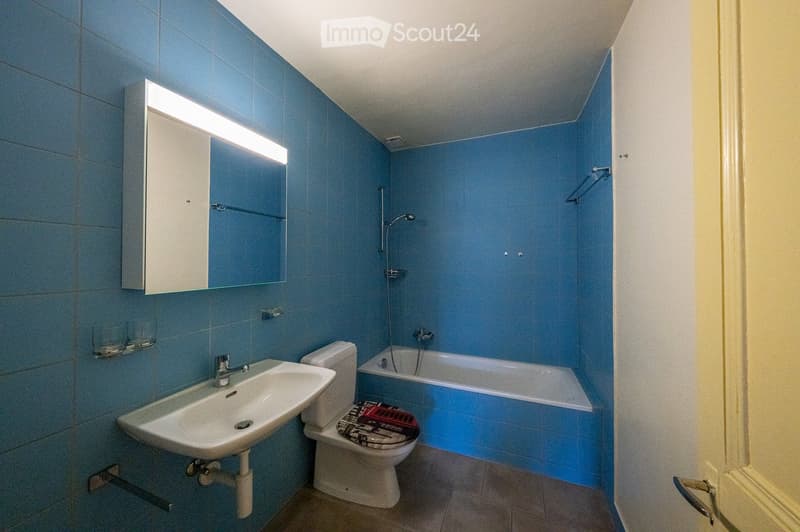 Bathroom with blue tiled walls, a white sink, toilet, bathtub, and a mirrored cabinet with a built-in light.