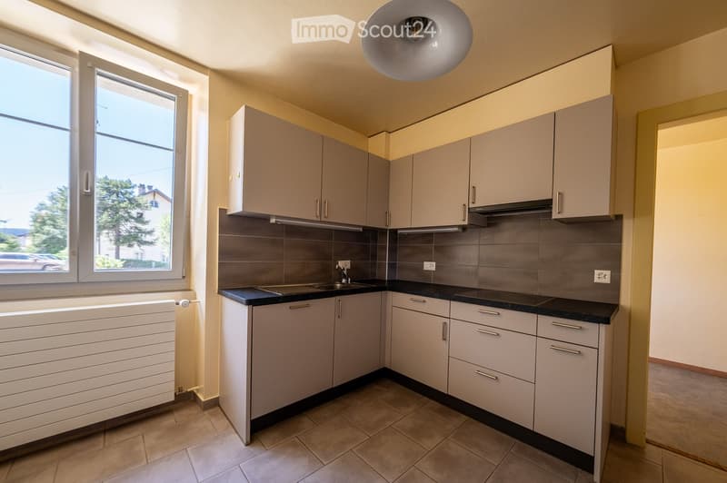 Modern kitchen with light grey cabinets, black countertops, tiled backsplash, and a window overlooking a street.