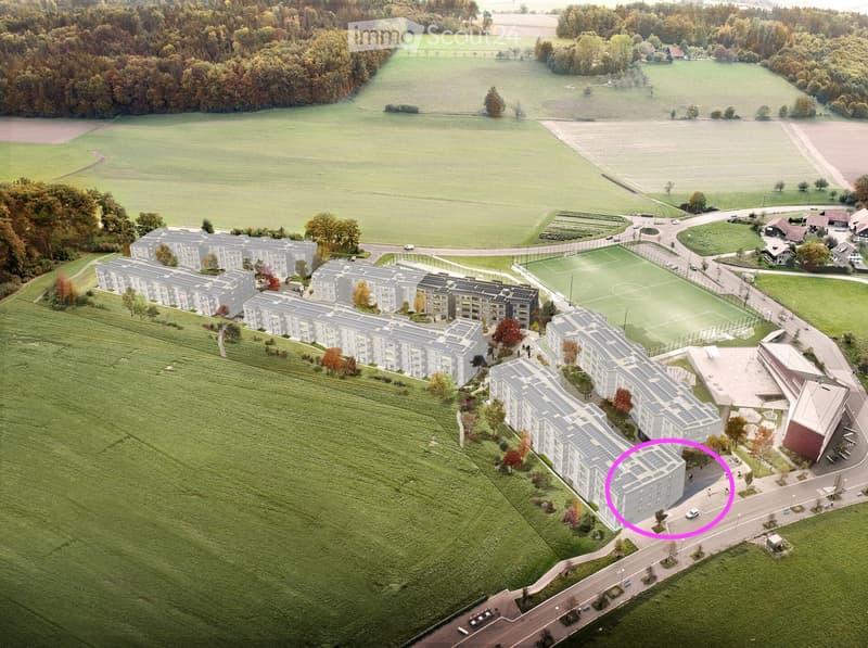 Aerial view of a residential complex with multiple apartment buildings, surrounded by green fields and a soccer field.