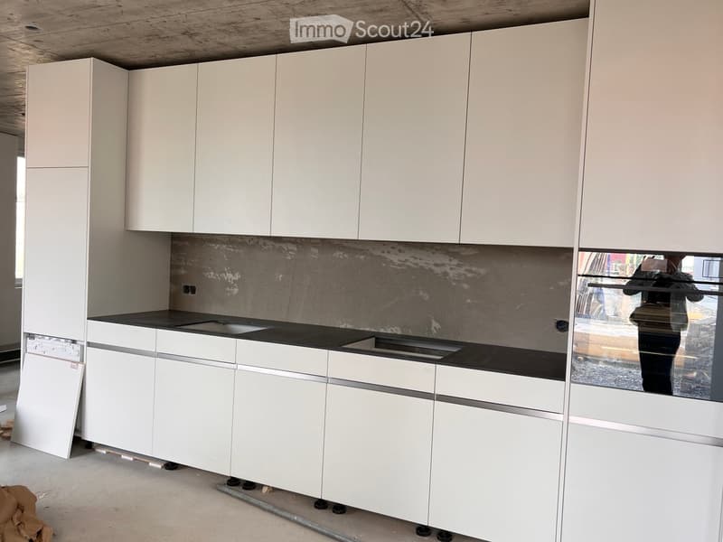 Modern kitchen with white cabinets, black countertop, and a sink, featuring a textured backsplash.